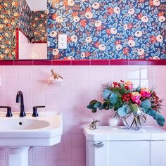 a bathroom with floral wallpaper and pink tiles on the walls, two sinks and a toilet