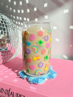 a cake in a glass on top of a pink table with a disco ball behind it