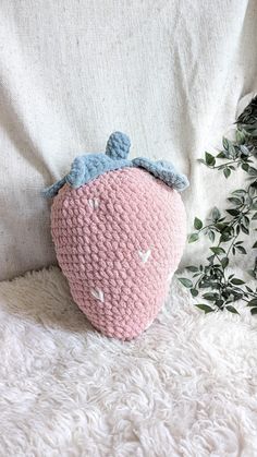 a crocheted strawberry sitting on top of a white blanket next to a plant