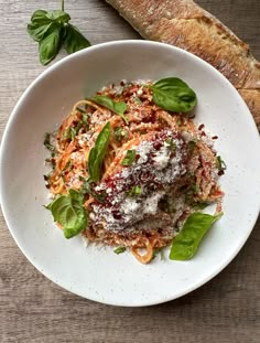 a white plate topped with pasta covered in sauce and greens next to a loaf of bread