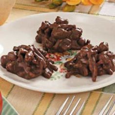 three pieces of chocolate covered cookies on a plate with forks and spoons next to it