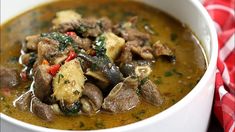 a white bowl filled with soup and meat on top of a red table cloth next to a wooden spoon