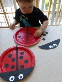 a little boy sitting at a table with two paper plates shaped like ladybugs