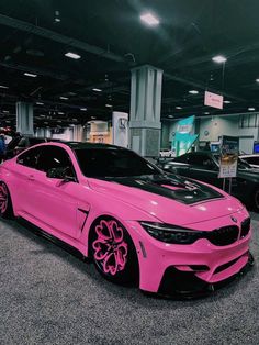 a pink car is parked in a showroom with other cars and people looking at it