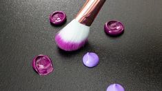 a close up of a makeup brush with purple eyeshades on a black surface