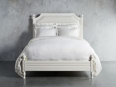 a bed with white linens and pillows against a gray wall in an empty room