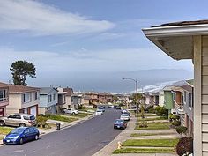 cars are parked on the street in front of houses near the beach and ocean with mountains in the background