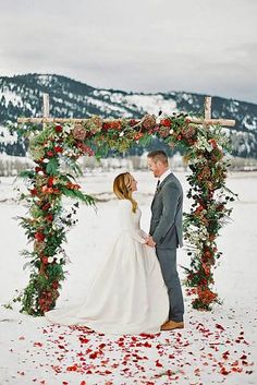 a bride and groom standing under an arch with flowers on it in the snow at their wedding