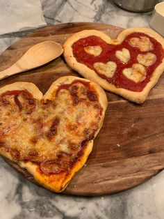 two heart shaped pizzas sitting on top of a wooden cutting board