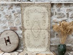 two vases with dried plants in front of an old rug on a stone wall