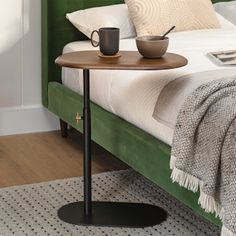 a bed with a green headboard and white sheets on it, next to a table with a coffee cup