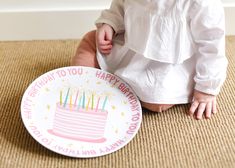 a baby sitting on the floor next to a birthday cake plate