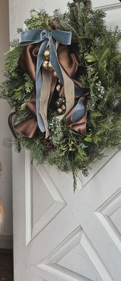 a wreath hanging on the front door of a house with blue ribbon and bells attached to it