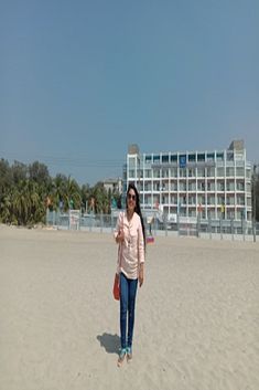 a woman standing on top of a sandy beach next to a tall white hotel building