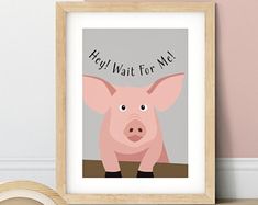 a pink pig sitting on top of a wooden table next to a framed poster with the words hey wait for me