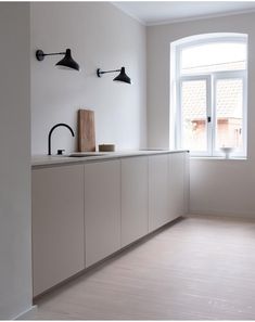 an empty kitchen with white cabinets and black lights on the windowsill, next to a large window