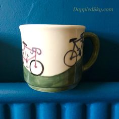 a coffee cup that is sitting on a shelf next to a radiator with two bicycles painted on it