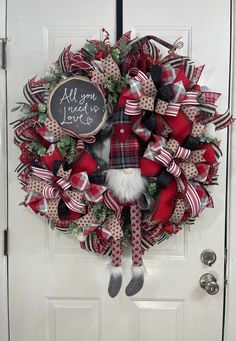 a red and black christmas wreath on a white door with the words all you need is love written on it