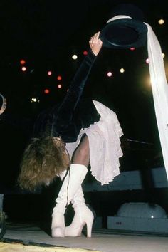 a woman in white boots is dancing with her hat over her head while holding onto a pole