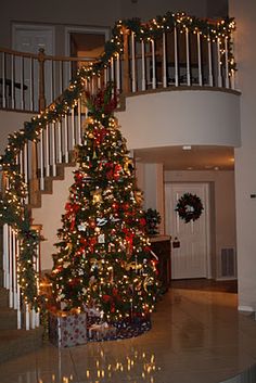 a decorated christmas tree in the middle of a living room with stairs and railings