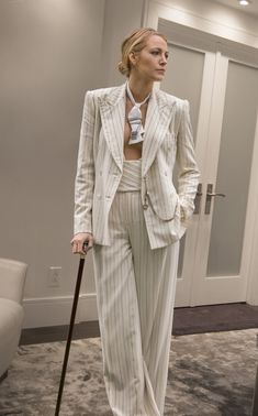 a woman in a white suit is standing with a cane and looking off to the side