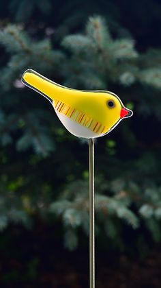 a yellow bird sitting on top of a metal pole next to a forest filled with trees