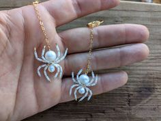 a hand holding two white spider earrings on it's fingers