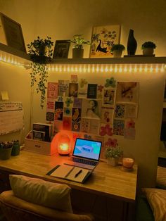 a laptop computer sitting on top of a wooden desk next to a lamp and potted plant