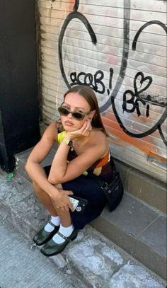 a woman sitting on the ground in front of a graffiti covered wall talking on her cell phone