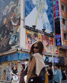 a woman standing in front of a tall building with posters on it's side