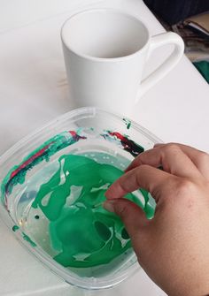 a person is painting with green paint on a white surface next to a cup and saucer