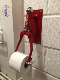 a red toilet paper dispenser hanging on the wall next to a roll of toilet paper