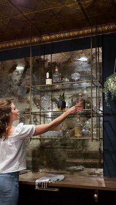 a woman is reaching for some flowers in a vase on a shelf with shelves behind her