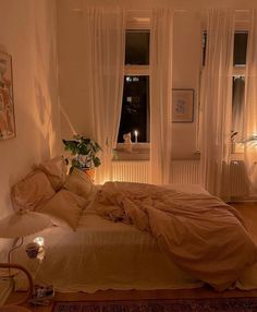 an unmade bed in a bedroom with candles on the windows sill and curtains