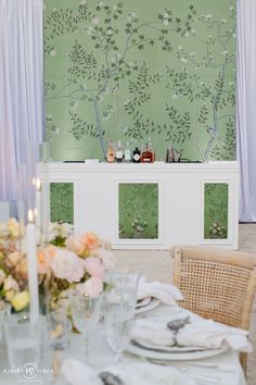 a dining room table set with place settings and flowers on the wall behind glass doors