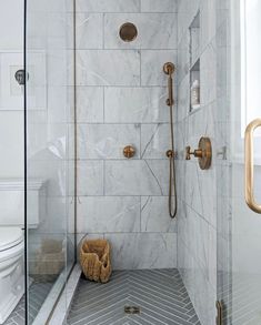 a walk in shower sitting next to a toilet and a white tiled wall with gold fixtures