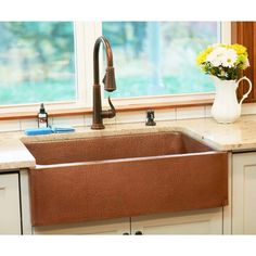 a kitchen sink sitting under a window next to a white vase with flowers in it