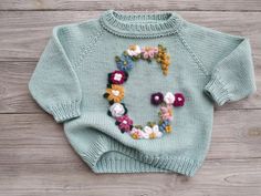 a knitted sweater with flowers on the front and back, sitting on a wooden surface