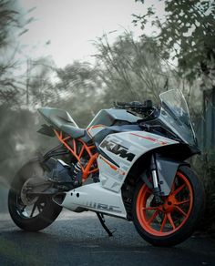 an orange and white motorcycle parked on the side of a road next to some trees