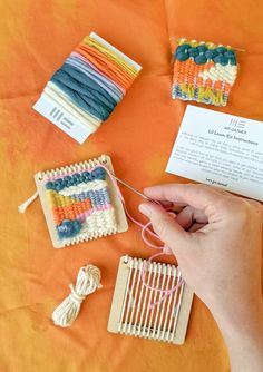 a person is knitting on an orange surface with several different types of yarns and crochet hooks