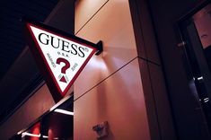 a sign hanging from the side of a building that says guess under a question mark