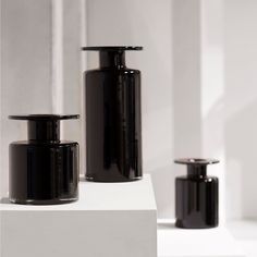 three black vases sitting on top of a white shelf next to eachother