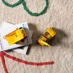 two yellow toy trucks sitting on top of a white carpet next to a red and green string