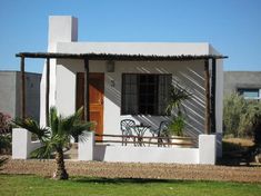 a small white house with a table and chairs on the front porch next to palm trees