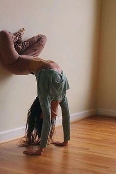 a woman doing a handstand on the floor in front of a white wall