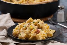 a black plate topped with macaroni and cheese next to a pot of pasta