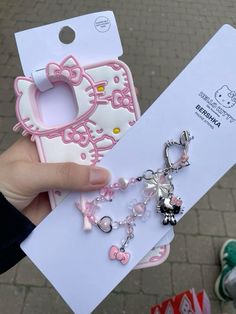 a person holding up a hello kitty phone case with charms attached to the back of it