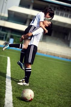 two young men are playing soccer on the field in front of an empty stadium building