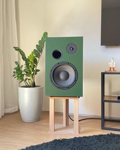 a green speaker sitting on top of a wooden stand next to a potted plant