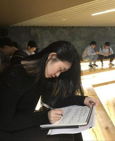 a woman is writing in a notebook while other people are sitting on the floor behind her